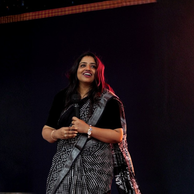 Woman in a black and white patterned saree standing on a dark background