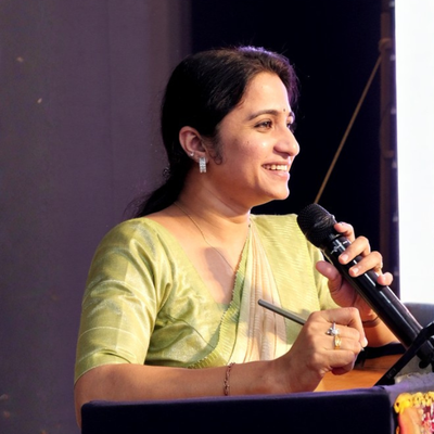 Woman in a green saree holding a microphone on a stage