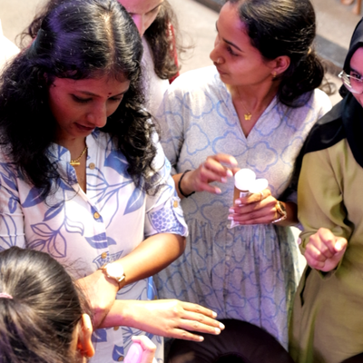 Group of women gathered around a woman applying cream to her hand.