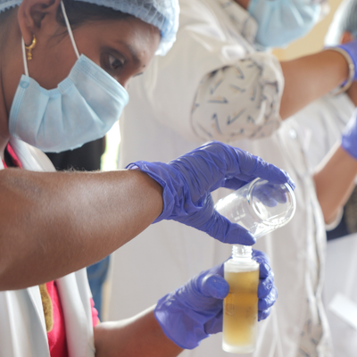 Person wearing gloves and a mask holding a bottle with a liquid substance.