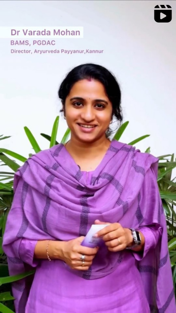 Woman in a purple traditional outfit holding Bakuchi Serum Moisturizer with greenery in the background